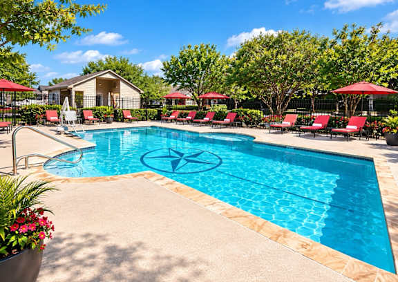 A pool surrounded by red lounge chairs and umbrellas.
