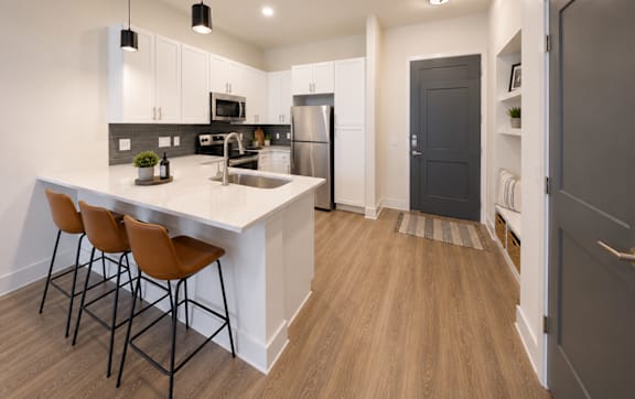 Designer kitchen with quartz countertops, white cabinetry, stainless steel appliances, and breakfast bar at The Mill Old Town Apartments.