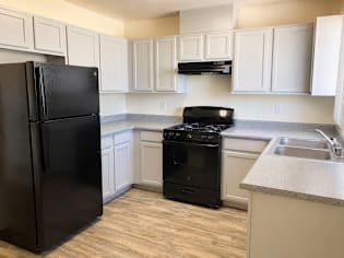 A black refrigerator stands in a kitchen with white cabinets.