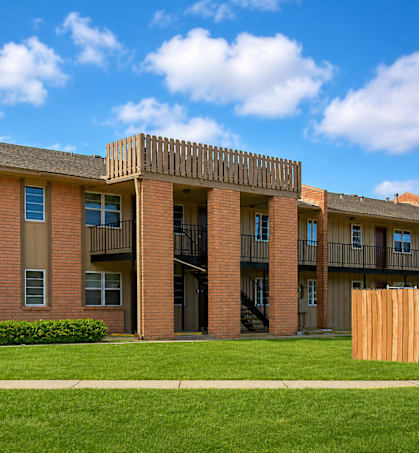 A red brick building with a balcony and a green lawn in front.