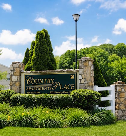 A sign for Country Apartments Place is surrounded by greenery.