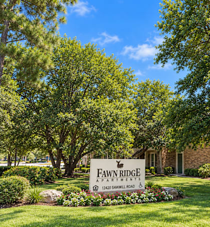 A sign for Fawn Ridge Apartments is in front of a building and trees.