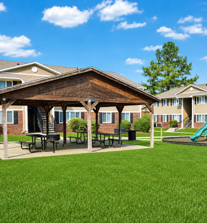 A playground with a green slide and picnic tables in front of a building.