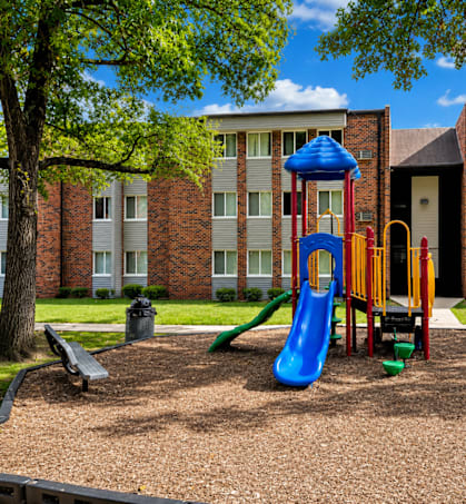 A playground with a blue slide and a yellow slide in front of a brick building.