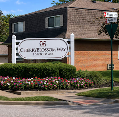 A sign for Cherryblossom Way townhomes stands in front of a brick building.