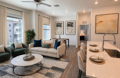 A modern living room with a white sofa set, a coffee table, and a kitchen area with a sink and countertop.