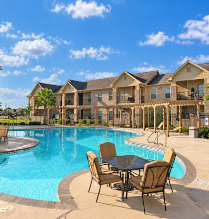 A swimming pool with chairs around it in front of apartment buildings.
