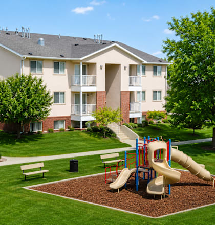 A playground with a slide and a bench in front of a building.