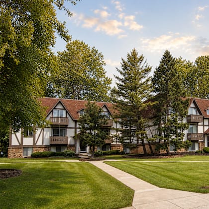A large, two-story building with a balcony on the second floor is surrounded by a well-manicured lawn and trees.