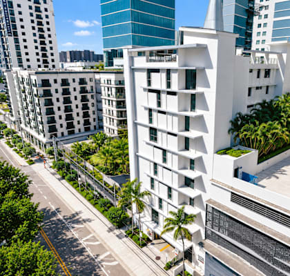 A modern white building with balconies is in the foreground with other buildings in the background.