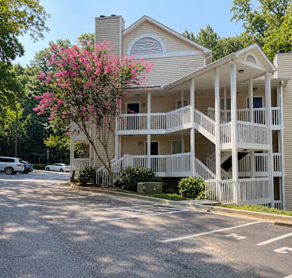 A two-story building with a balcony and a tree with pink flowers in front.