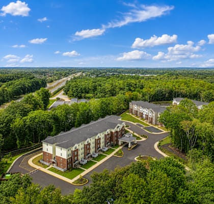 A large building surrounded by trees with a parking lot in front.