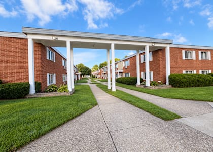A long white covered walkway leads to a building with a row of red brick houses on either side.