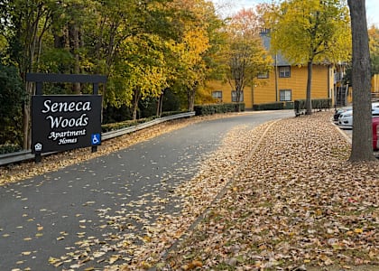 A sign for Seneca Woods Apartments is in front of a yellow building.