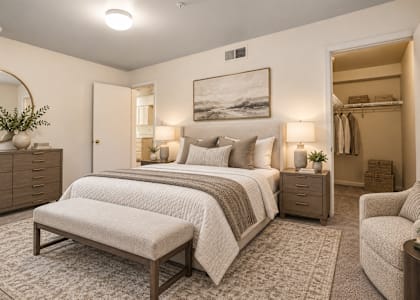 A well-lit bedroom with a large bed, a bench, and a chair.