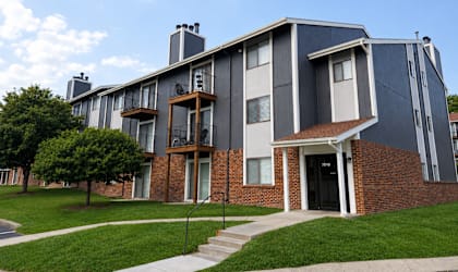 A modern two-story apartment building with a brick facade and a balcony on the second floor.