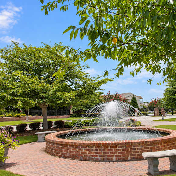 A fountain in the middle of a brick circle with benches around it.