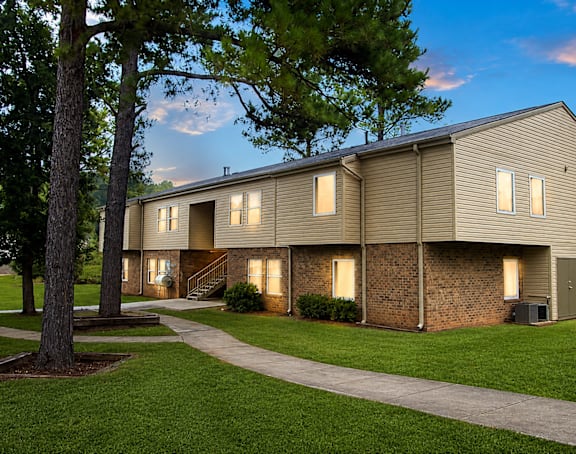 A building with a brown siding and a brick wall is surrounded by a grassy area and trees.