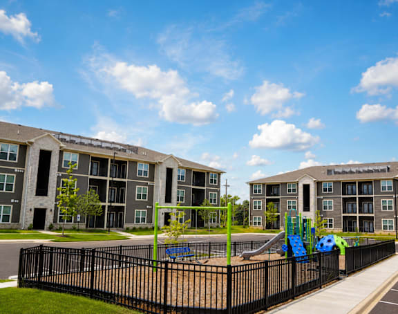 A playground with a slide is in front of apartment buildings.