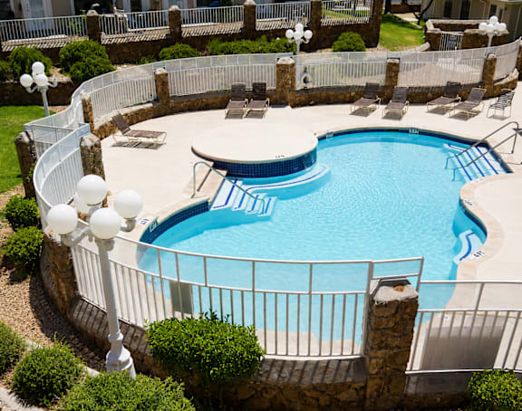 A round swimming pool surrounded by a fence and a stone wall.