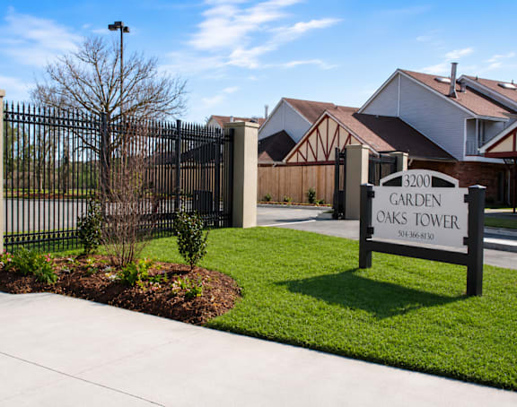 A sign for Garden Oaks Tower is in front of a black gate.