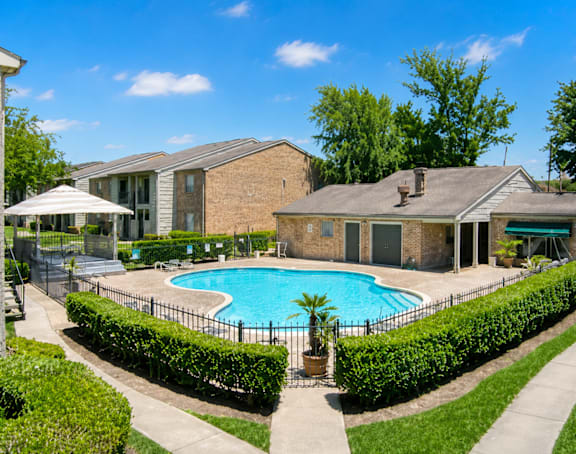 A pool surrounded by a black fence and green bushes.