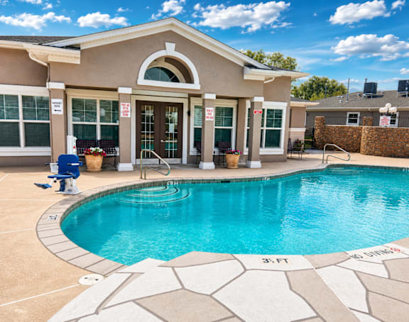 A swimming pool in front of a house with a blue sky in the background.