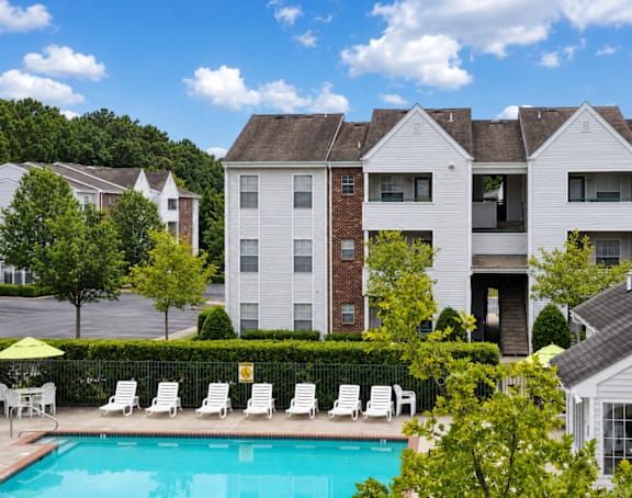 A pool in front of a white and brick building with a yellow umbrella.