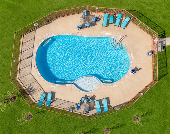 An aerial view of a swimming pool surrounded by a fence and lounge chairs.