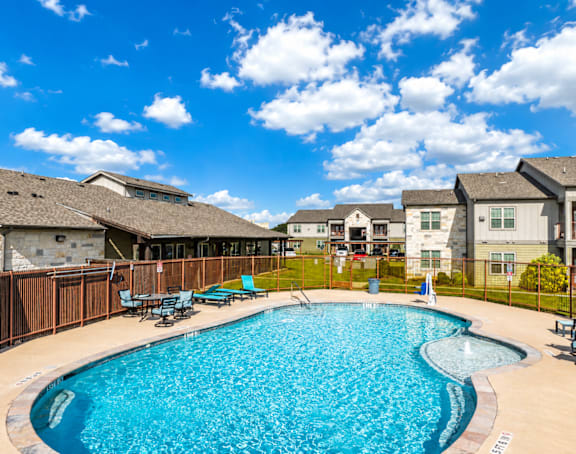 A swimming pool surrounded by a wooden fence and chairs.