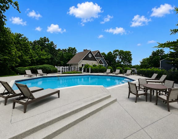 A pool surrounded by chairs and a house in the background.