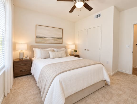 A bedroom with a large bed, two lamps, and a painting on the wall.