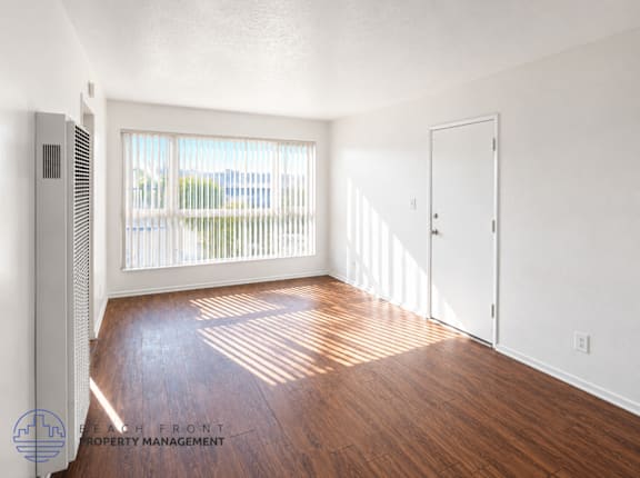 A room with wooden floors and white walls, with a window and a door visible.