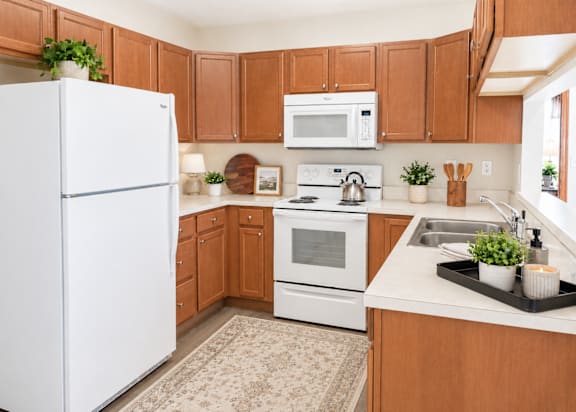 A white refrigerator stands in a kitchen with brown cabinets and a white stove.