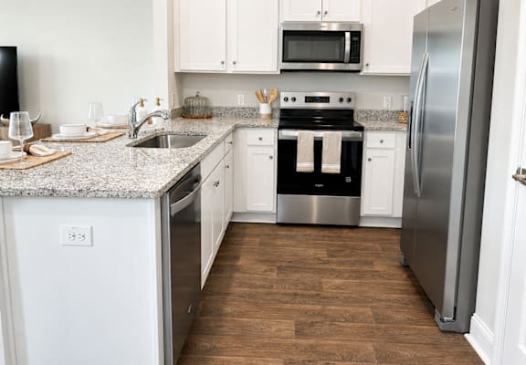 A kitchen with a stainless steel refrigerator, a microwave above the stove, and a sink with a granite countertop.