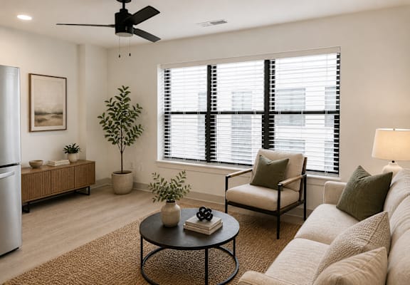 A living room with a sofa, a table, a plant, and a fan.