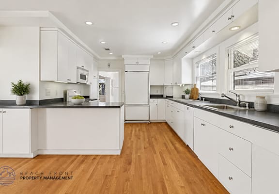A modern kitchen with white cabinets and wooden floors.