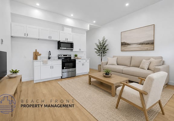 A modern kitchen with white cabinets and appliances, a wooden coffee table, and a beige sofa with a painting on the wall.
