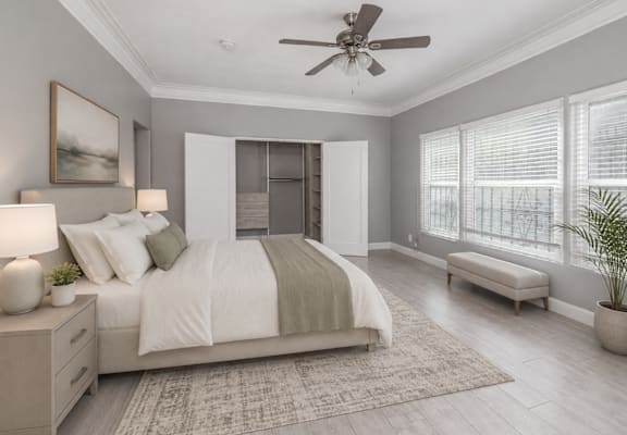 A bedroom with a large bed, a ceiling fan, and a window with blinds.