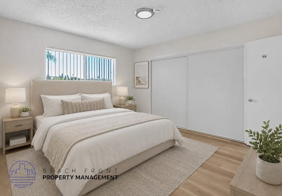 A bedroom with a large bed, a nightstand with lamps, a window with blinds, a rug, a potted plant, and a sliding door.