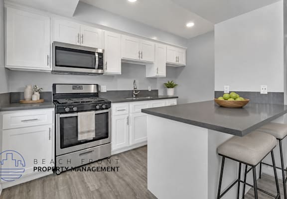 A modern kitchen with a stove, oven, microwave, and bar stools.