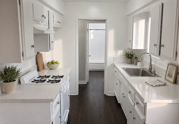 A white kitchen with a stove, sink, and cabinets.