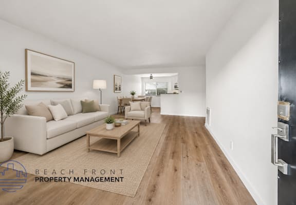 A spacious living room with a white couch, wooden coffee table, and a painting on the wall.