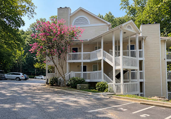 A two-story building with a balcony and a tree with pink flowers in front.