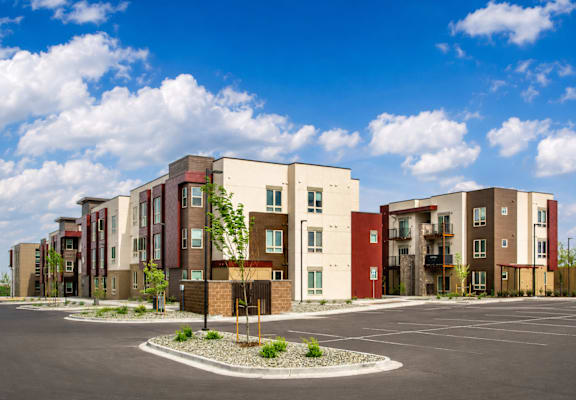 A row of modern apartment buildings with a parking lot in front.