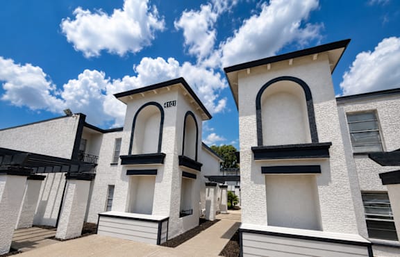 A white building with black trim and a black roof is shown under a blue sky with clouds.