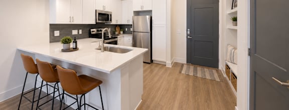 Designer kitchen with quartz countertops, white cabinetry, stainless steel appliances, and breakfast bar at The Mill Old Town Apartments.