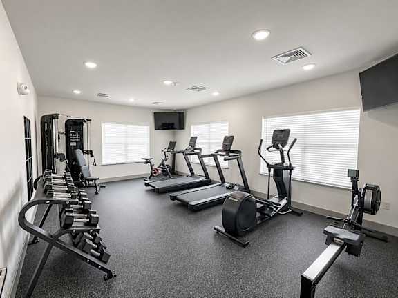 A spacious gym with treadmills, elliptical machines, and dumbbells.