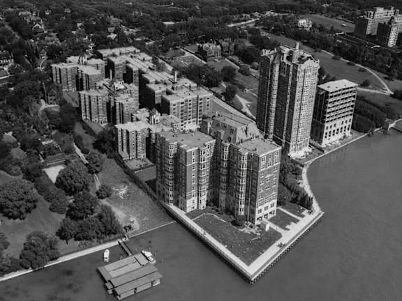 A black and white aerial view of a city with tall buildings, a body of water, and a boat.