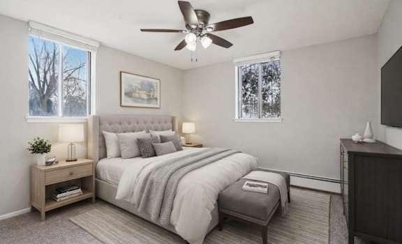 A bedroom with a large bed, a ceiling fan, and a window with a view of trees outside.